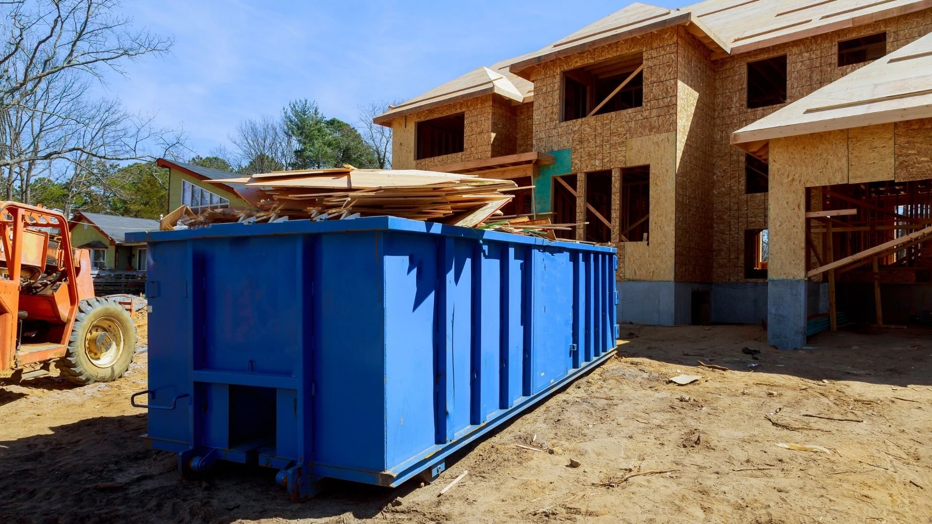 Blue dumpster at construction site with brick home under development in background