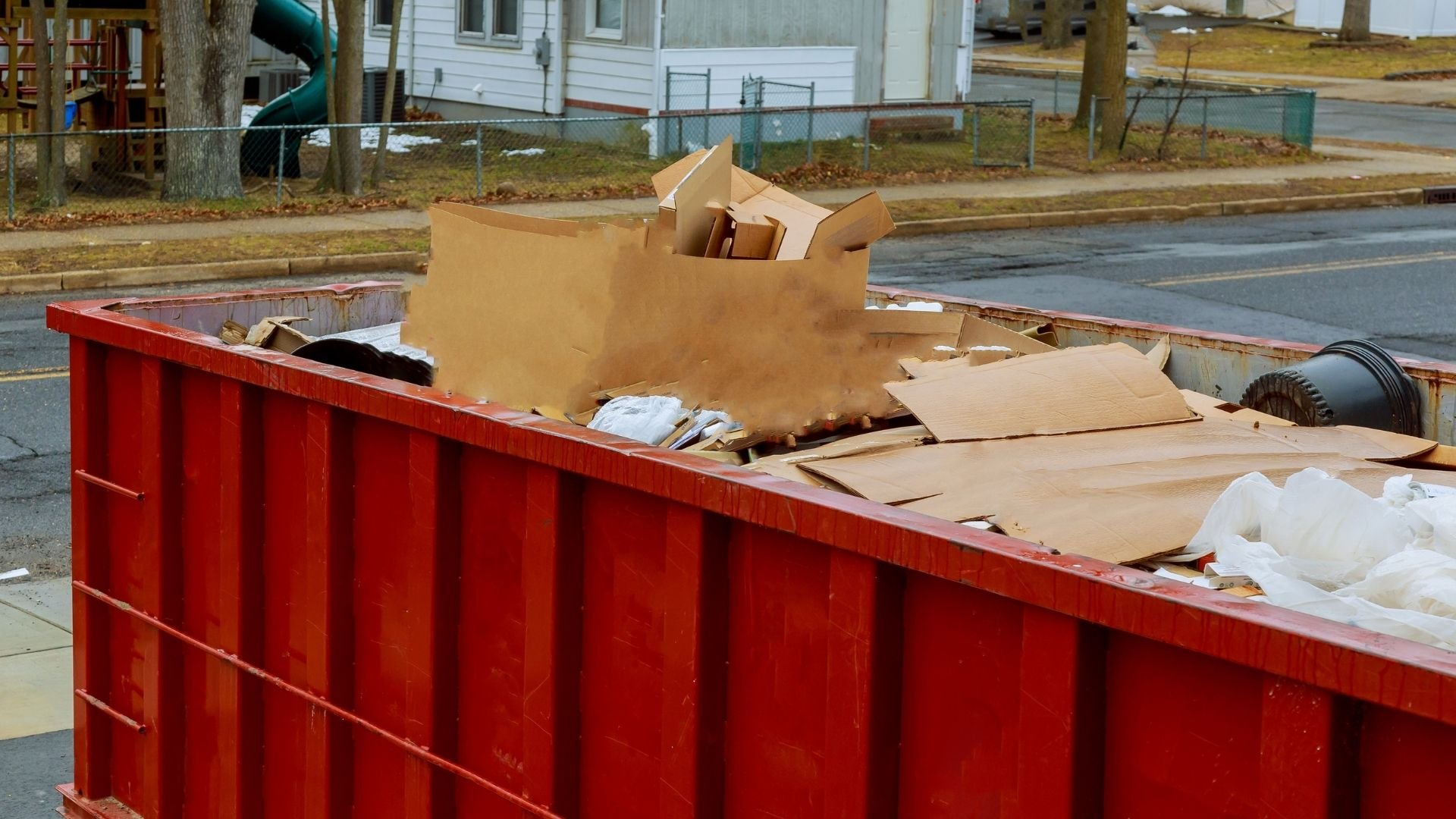 Red dumpster filled with cardboard boxes, wood, and miscellaneous waste on residential street