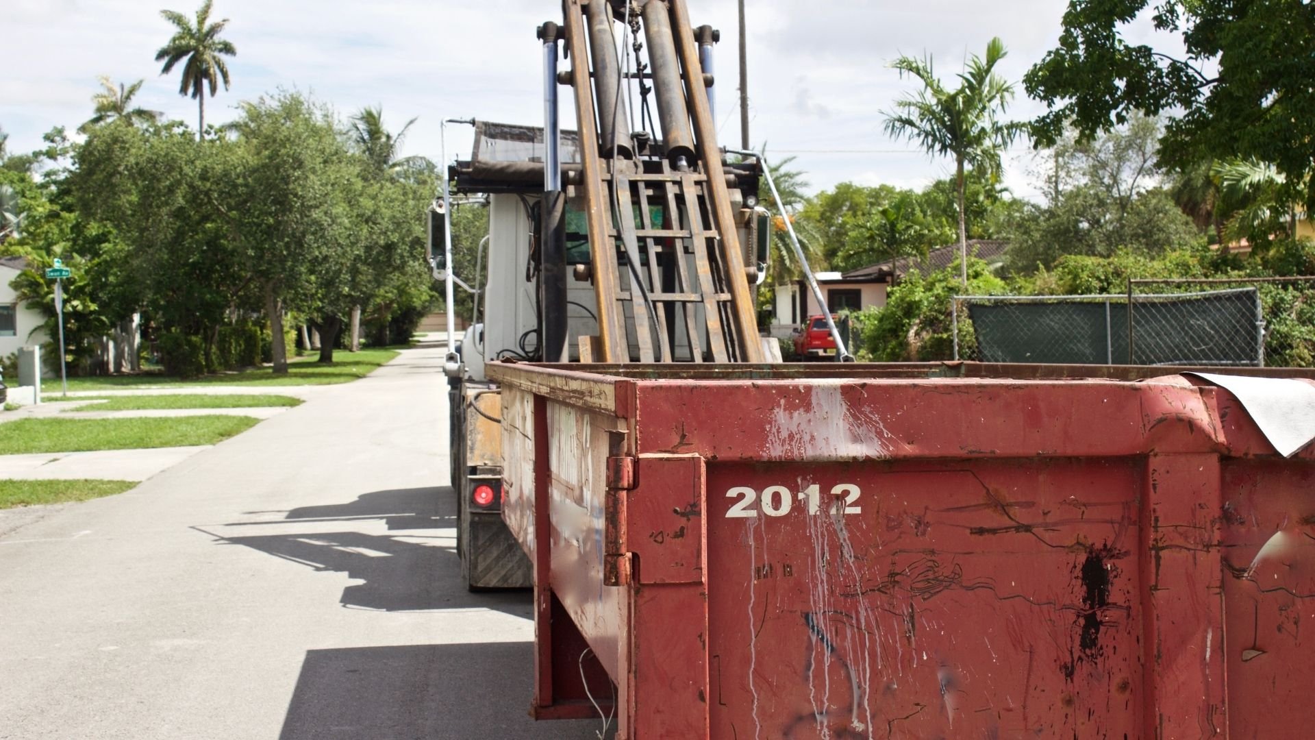Red dumpster truck loaded with metal materials parked on residential street.