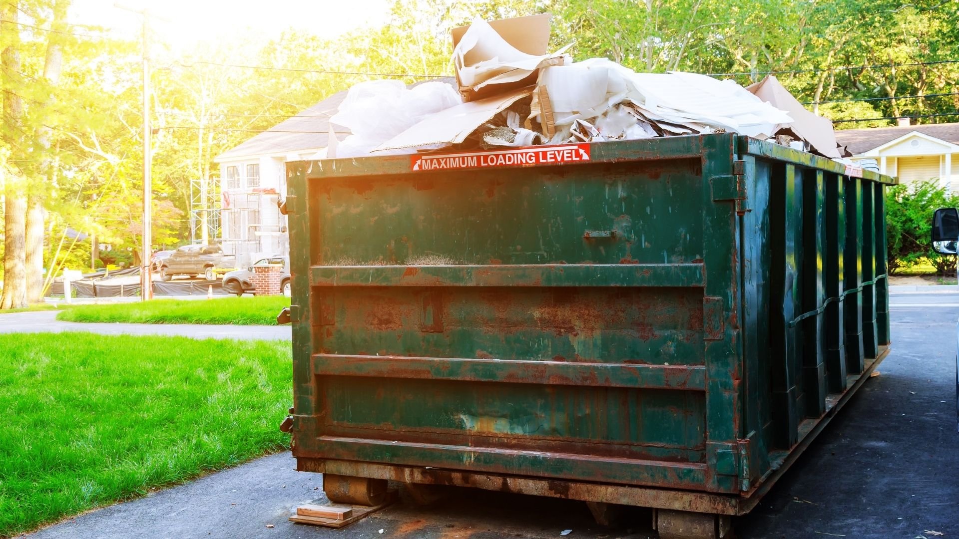 Overflowing green dumpster filled with cardboard and paper waste on residential driveway