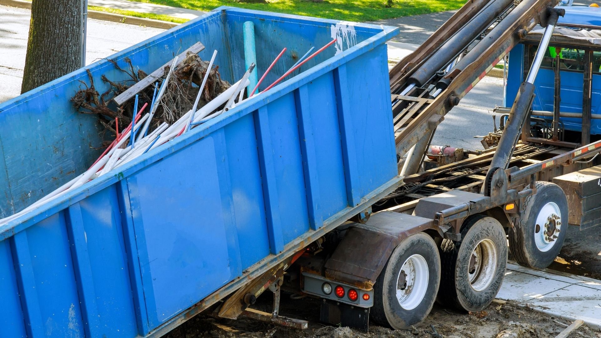Blue dumpster filled with debris and pipes on construction truck