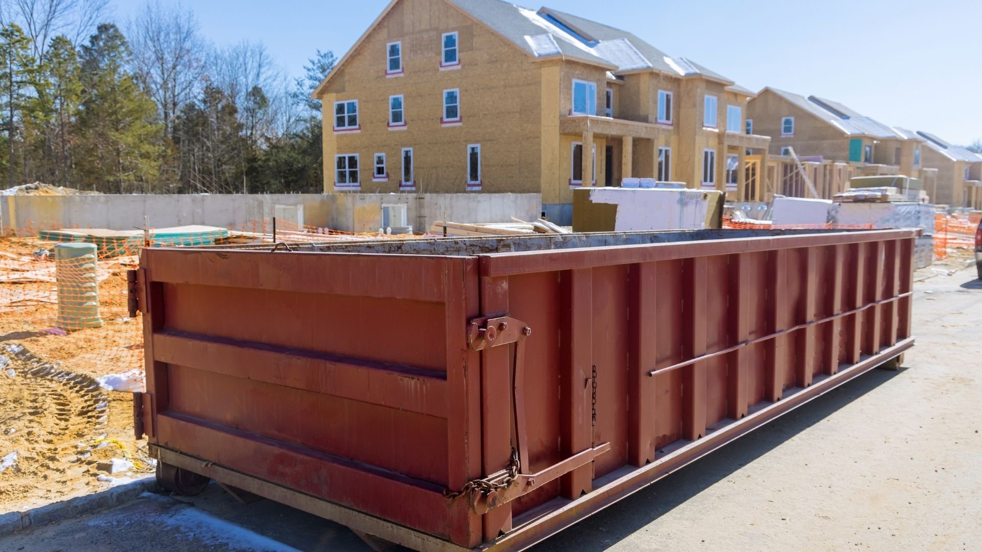 Large red dumpster at residential construction site with yellow houses under development