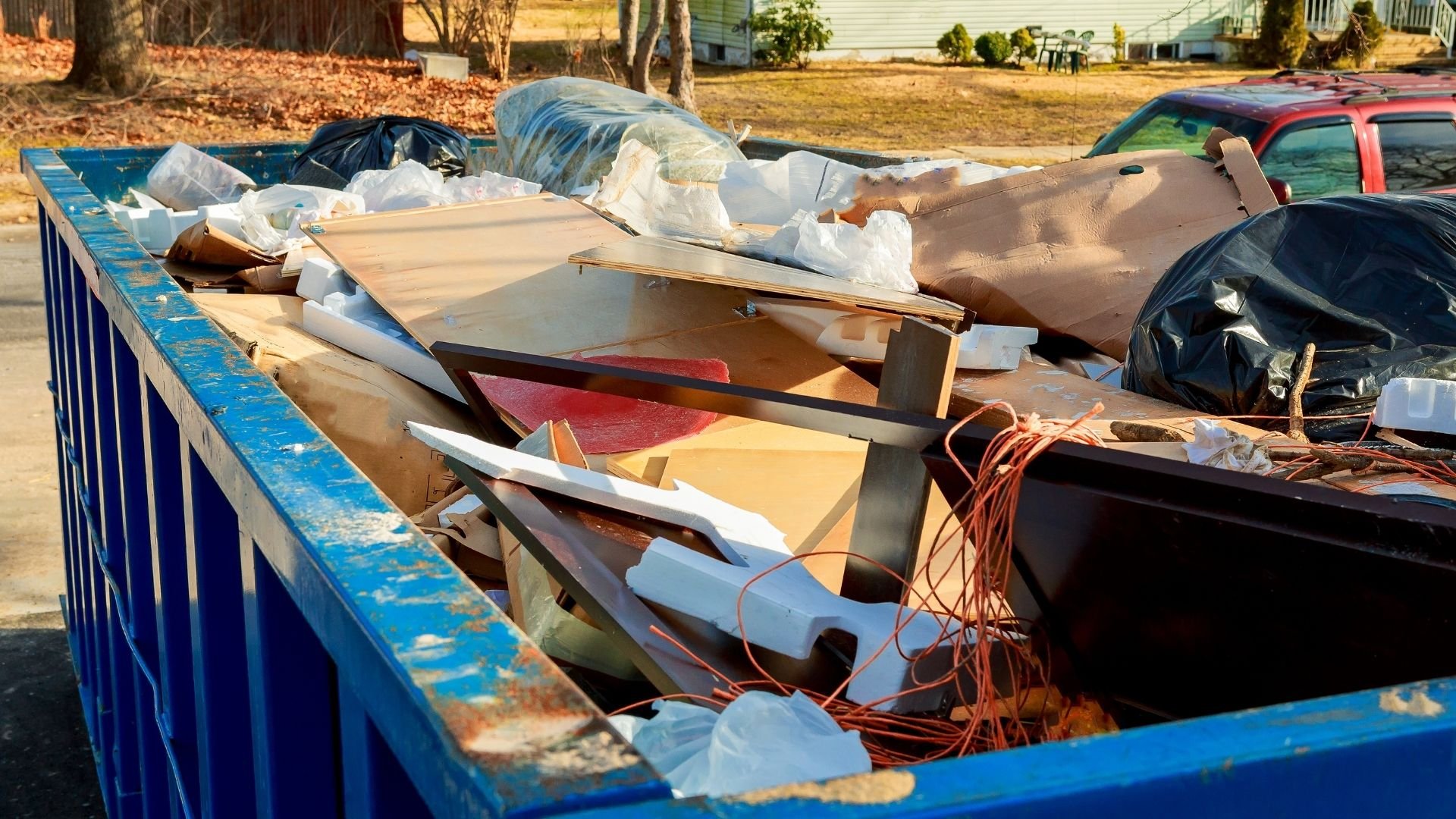 Blue dumpster overflowing with construction waste, wood, and debris in residential area